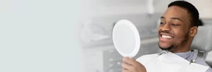 man in dental chair holding mirror smiling